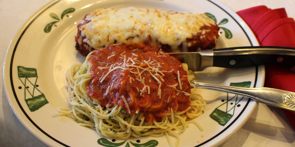 close up shot of pasta with red sauce and chicken parmesan