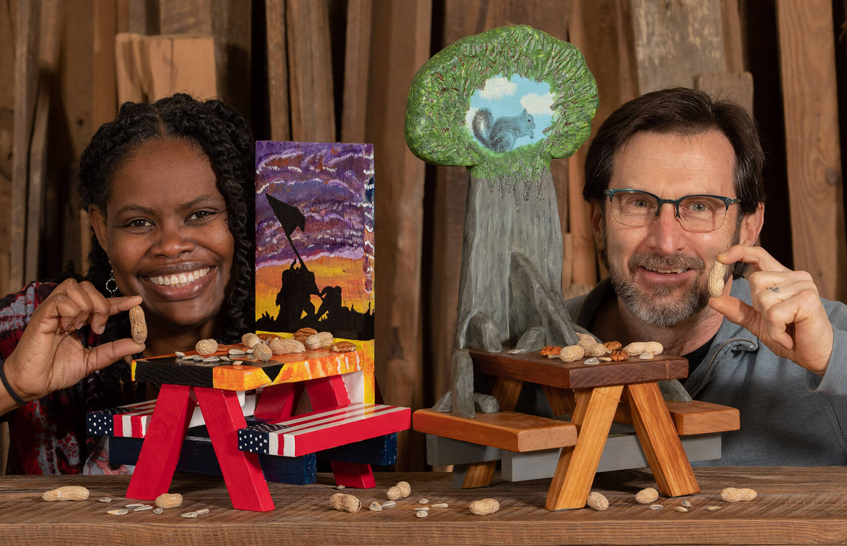 two people hold peanuts and pose behind small painted picnic tables