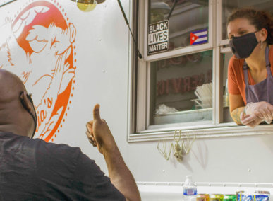 Woman in mask leans out food truck window to talk to customer