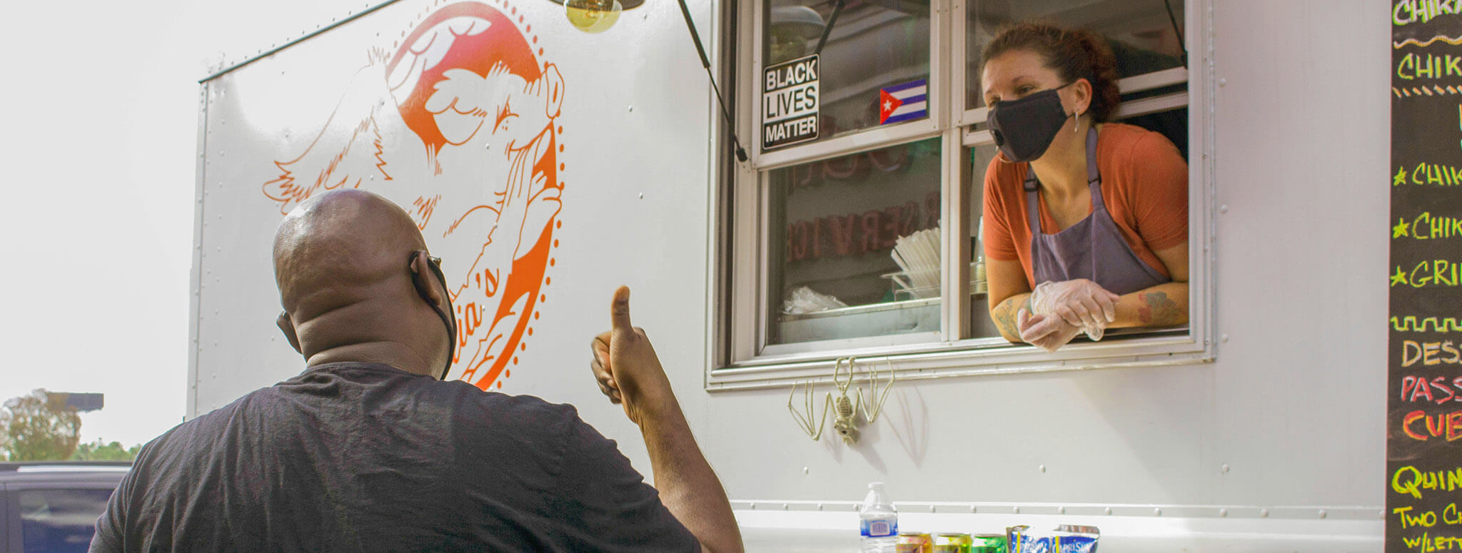 Woman in mask leans out food truck window to talk to customer