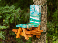 tiny picnic table painted with green and white swirls and mounted to a tree