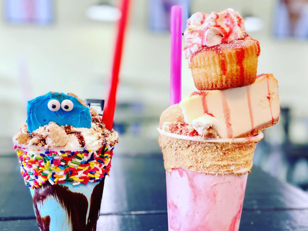 two extreme milkshakes - one with a cookie monster cookie and one with a piece of cheesecake and cupcake