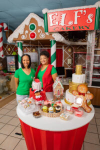 two women stand behind table filled with baked goods