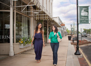 two women walk down a mainstreet past a restaurant