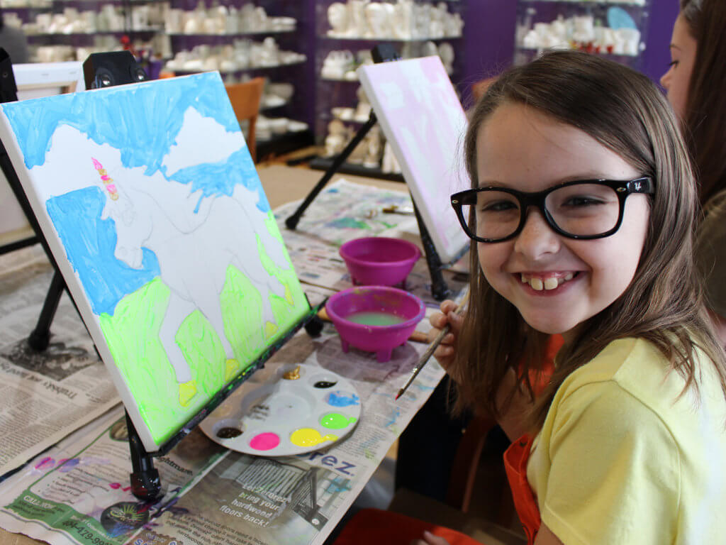 little girl canvas painting and smiling at camera