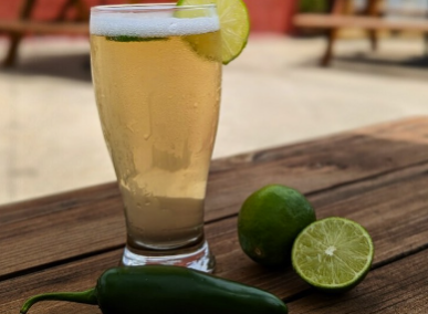 A glass of liquid with limes and a slice of lime on a wooden table
