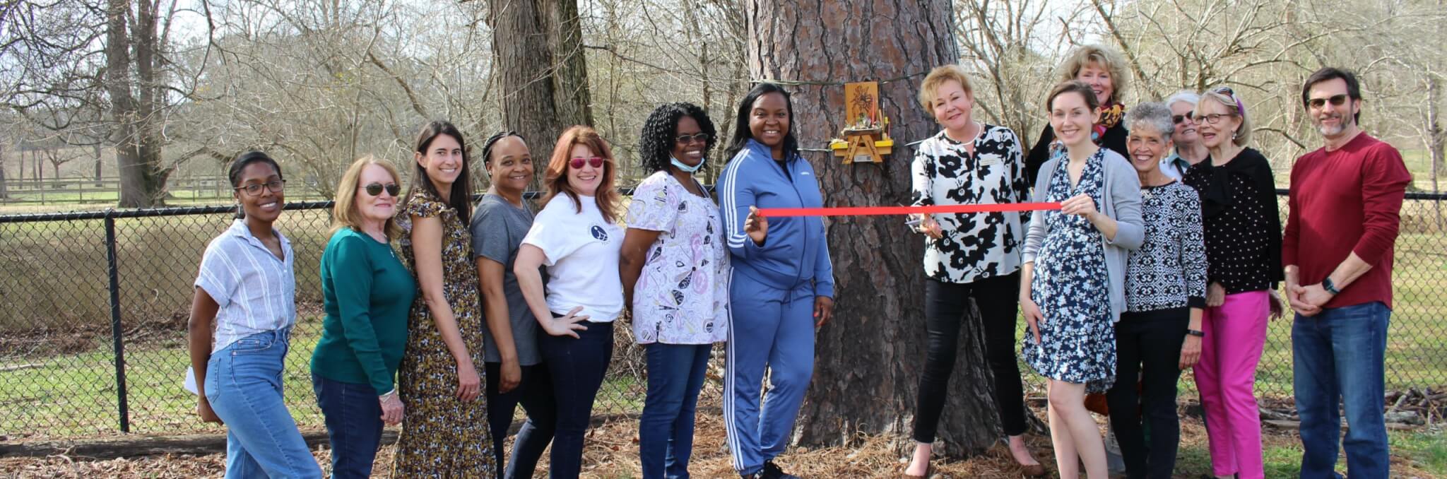 Group photo of ribbon cutting in front of small picnic table mounted to tree