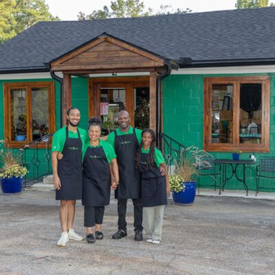 four people stand in front of a green building